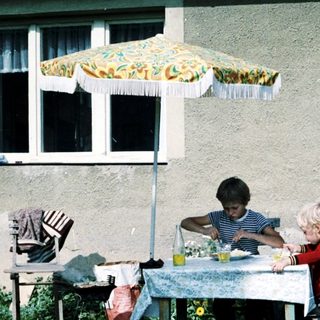 Two children eating outdoors under umbrella.