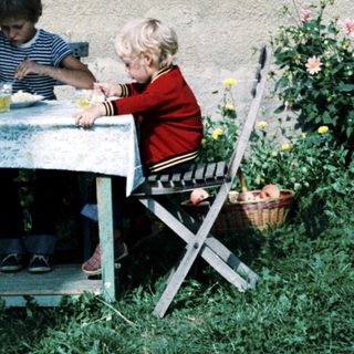 Two children eating outdoors under umbrella.