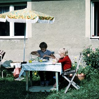 Two children eating outdoors under umbrella.