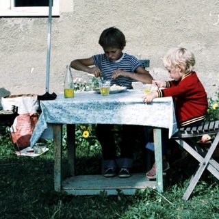 Two children eating outdoors under umbrella.