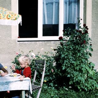 Two children eating outdoors under umbrella.