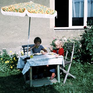 Two children eating outdoors under umbrella.