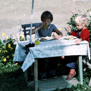 Two children eating outdoors under umbrella.