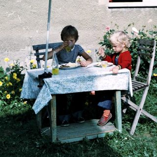 Two children eating outdoors under umbrella.