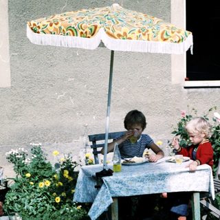 Two children eating outdoors under umbrella.
