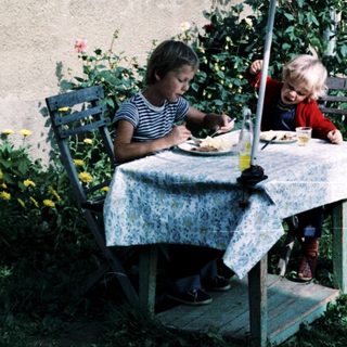 Two people eating outdoors under umbrella.