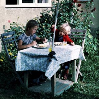 Two people eating outdoors under umbrella.