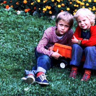 Two children sitting on grass with toy truck.