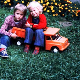 Two children sitting on grass with toy truck.