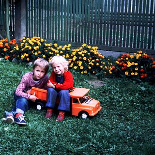 Two children sitting on grass with toy truck.