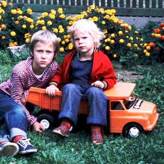 Two children sitting on grass with toy truck.
