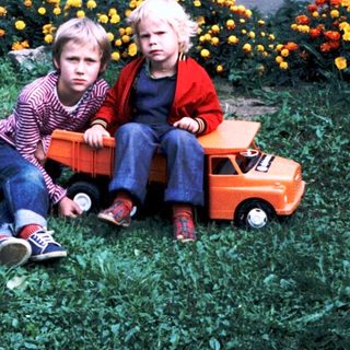 Two children sitting on grass with toy truck.