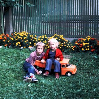 Two children sitting on grass with toy truck.