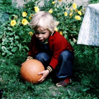 Woman sitting outdoors with child playing ball.