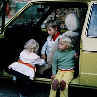 Three children sitting in open car doors.