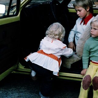 Three children sitting in open car doors.