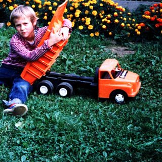 Boy playing with toy truck in grassy area.