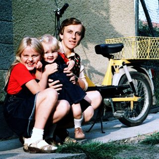 Family posing together outdoors near a bicycle.