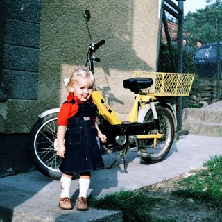 Young girl standing beside yellow moped.