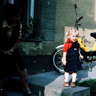 Young girl standing beside yellow moped.
