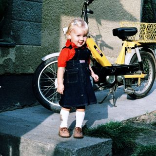 Young girl standing beside yellow moped.