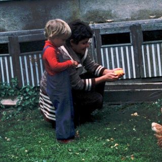 Two people feeding chickens in backyard coop.