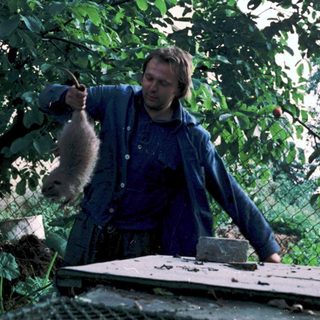 Man feeding a monkey outdoors near trees.
