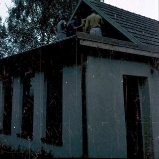 Two people repairing roof shingles on a house.