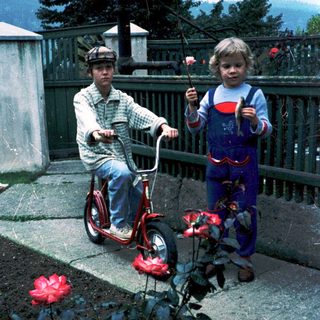 Two children on bikes in outdoor garden area.