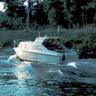 Child watches boat speeding on river near shore.