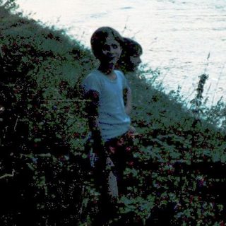 Child watches boat speeding on river near shore.