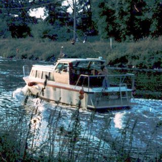 Two children by riverbank watching boat.