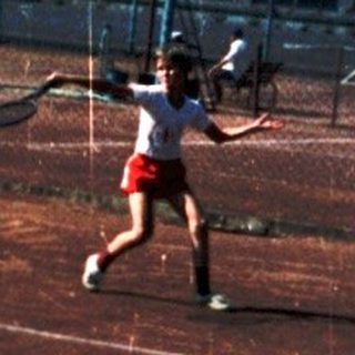 Person playing tennis on outdoor court.