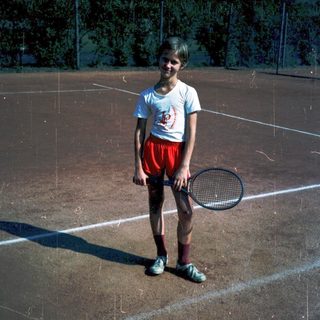 Young boy holding tennis racket on clay court.