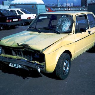 Yellow car with severe front damage, broken windshield.