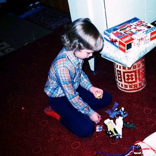 Child assembling toy camera on floor with gift boxes.