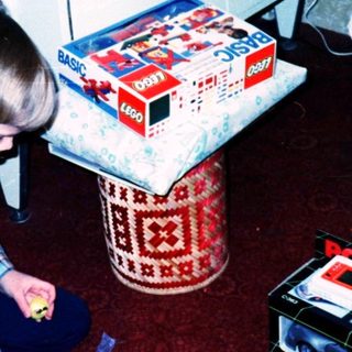Child assembling toy camera on floor with gift boxes.