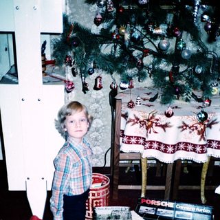 Child kneeling by Christmas tree with gifts.