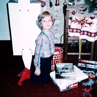 Child kneeling by Christmas tree with gifts.