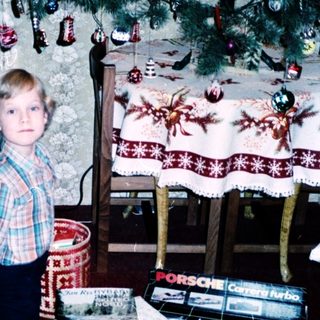 Child kneeling by Christmas tree with gifts.