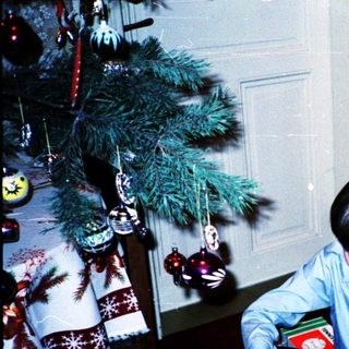 Child opening holiday gift beside decorated Christmas tree.