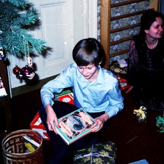 Child opening holiday gift beside decorated Christmas tree.