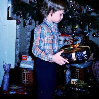 Child opening wrapped gift under decorated Christmas tree.