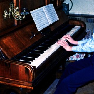 Young boy playing piano indoors with sheet music.