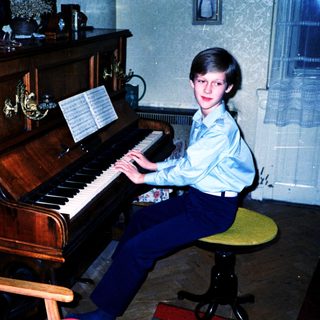Young boy playing piano indoors with sheet music.