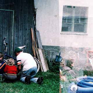 People repairing a motorcycle near a barn.
