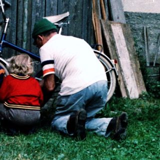People repairing a motorcycle near a barn.