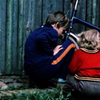 People repairing a motorcycle near a barn.