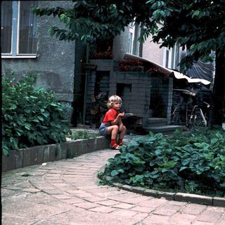 Child sitting outdoors near garden bed with adult nearby.