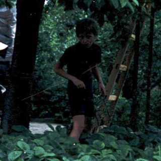 Child sitting outdoors near garden bed with adult nearby.